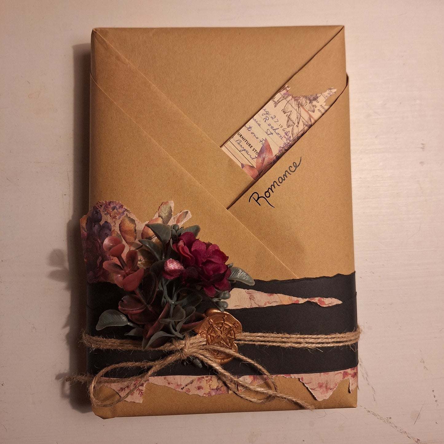 A romance book wrapped in brown paper with decorative ribbons and flowers